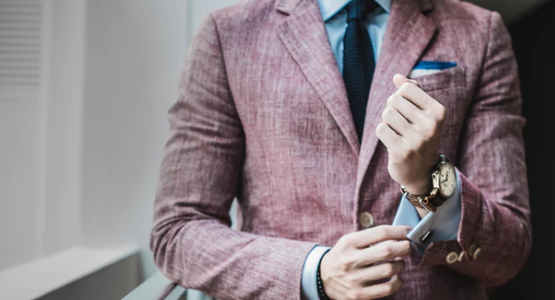 A man in a formal suit adjusting the cuffs of his shirt