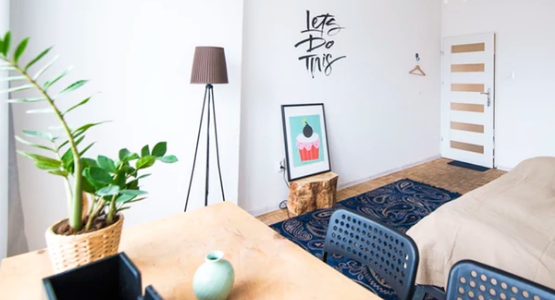 A bedroom with a lamp, sofa, bed, desk, plant, painting, and light fixture