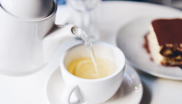 A person pouring a cup of tea into a teacup that has a lemon inside of it